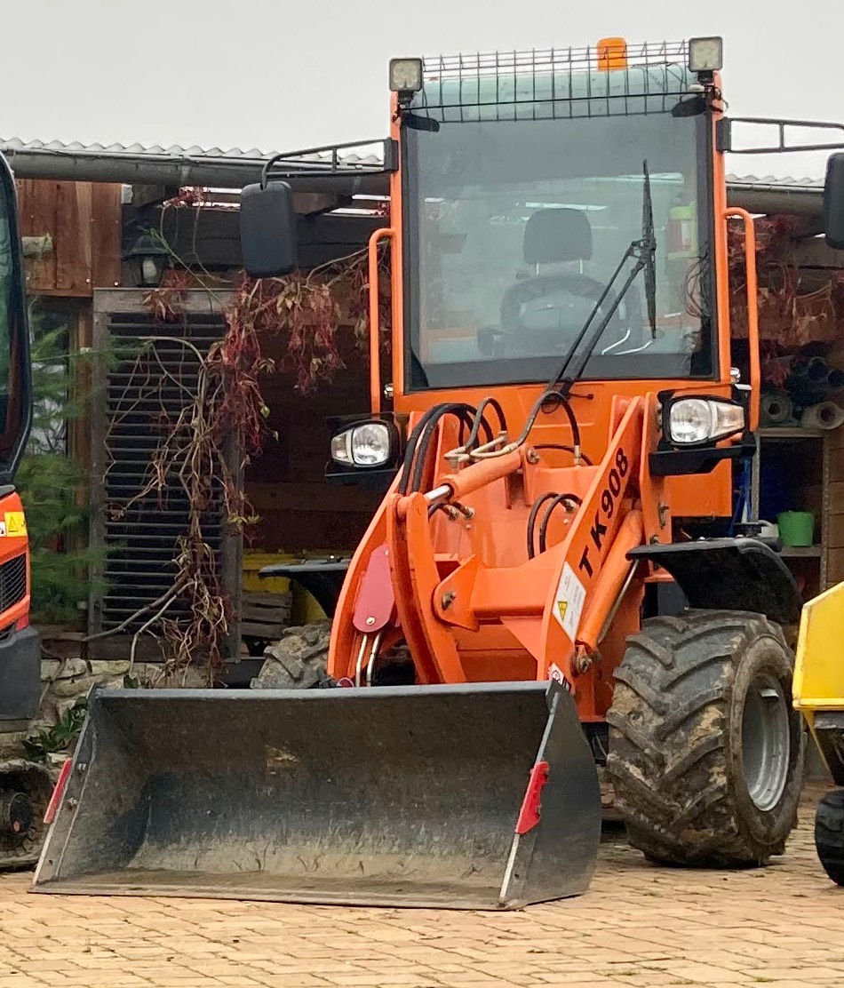 Orangefarbener Radlader mit Schaufel, von vorn gesehen.